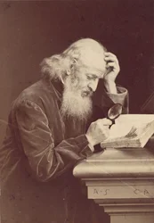[Skäggig man med förstoringsglas undersöker ett manuskript], 1870-talet.