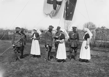 En grupp oidentifierade officerare, sjuksköterskor och män från 3rd Australian Casualty Clearing Station samlades under en flaggstång med den australiska flaggan (Australian Blue Ensign) och Röda Korsets flagga