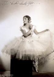 Porträtt av den klassiska ballerinan Rosa Piovella Ansaldo, i tutu och balettskor. Hon sitter framtill, ansiktet vänt åt sidan. Tykrosor pryder hennes plagg och omsorgsfullt klädda hår (Milan, Teatro alla Scala) (s/v foto)