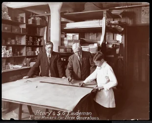 Porträtt av Henry och S.G. Lindeman med deras son eller barnbarn stående över butiksteckningar för ett piano, 1910 (silvergelatintryck)