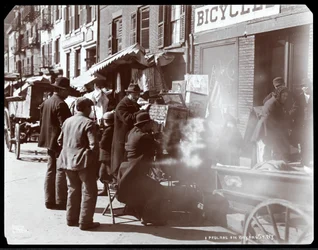 Vy över gatuförsäljare, bland annat en som visar fotografiska bilder av exotiska platser i en tittlåda, på Bayard Street, New York, 1898 (silvergelatintryck)