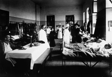 Inredd salong på sjukhus med krigsskadade, läkare, Röda Korsets sjuksköterskor och besökare (s/v foto)