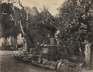 Lantlig scen med stenbyggnad och kors, ca. 1857.