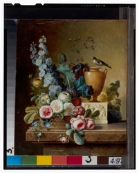En vas med blommor på en marmoravsats & en korg med blommor med en guldfink