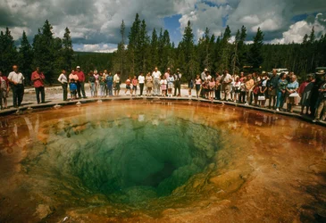 Parkbesökare samlas runt en blågrön, blomformad varm källa. Yellowstone nationalpark