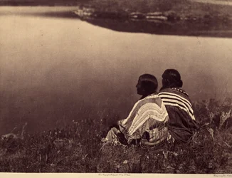 En ledig timme - ett ögonblick av lugn: Piegan indianer som sitter på kanten av en vattenmassa. Foto taget från volym 6 i Encyclopedia publicerad av Edward S. Curtis (1868-1952) på indianerna i Nordamerika, med ett förord av Theodore Roosevelt. B