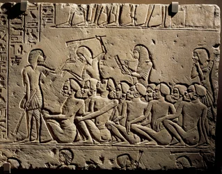 En grupp svarta fångar omgiven av vakter beväpnade med klubbor, medan en skrivare upprättar en rapport, relief från Horemhebs grav i Saqqara
