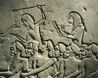 En grupp svarta fångar omgiven av vakter beväpnade med klubbor, medan en skrivare upprättar en rapport. Relief från Horemhebs grav i Saqqara, detalj