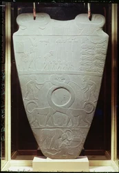 Narmerpaletten: ceremoniell palett som avbildar kung Narmer med Nedre Egyptens röda krona, inspekterande bundna och halshuggna fångar, samt ett par jättelika långhalsade katter, funnen i Hierakonpolis