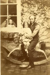 Far och dotter sitter på en gunghäst med bror och mor tittar genom fönstret, 1860-tal (albumintryck)