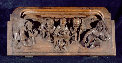 En misericord som föreställer en akademiker som sitter vid ett panelbord och levererar en förmaning till en knästående ångerfull, New College Chapel, Oxford, sent 1300-tal (trä)