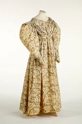 Klänning tryckt med blom- och grendesign på krämvävt tyg med rutmönster i väven, ca 1830-35 (bomull)