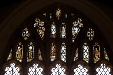 Fönster Ew som visar tracery-ljusen med Gud, Treenigheten, St Peter. St Paul, St Catherine och Gabriel: och en fågel