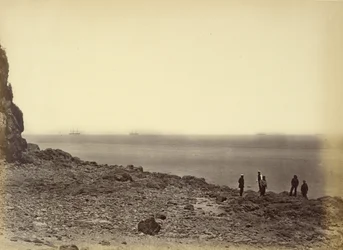 [Vy över stranden med fartyg i horisonten och fem personer som står på stranden]