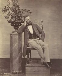 [Mathias Höusermann sittande med armbåge på piedestal med en vas med blommor], 1850-60-tal.