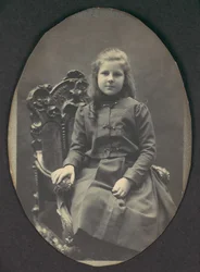[Flicka med ringlar, sittande, trekvartslängd], 1890-tal.