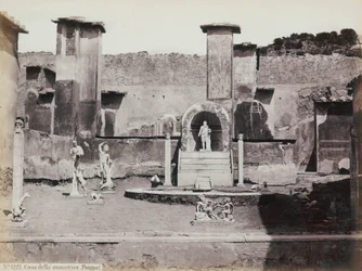 Delvis utsikt över den förhöjda trädgården till huset av Marcus Lucretius i Pompeji, dekorerad med marmorstatyer och herms. I mitten en fontän med en nisch. I bakgrunden fragment av väggmålningar