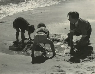 Tre barn leker med sand på stranden.