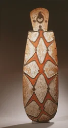 Oval Asmat-sköld, snidad i relief med stiliserade figurer, en mask upptill (trä)