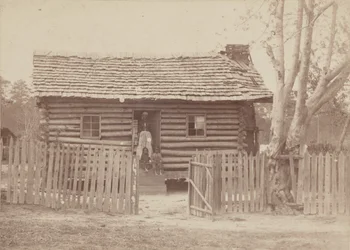 Albumintryck av en kvinna och två barn framför ett timmerhus i Georgia, 1880-talet.