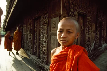 En ung nybörjarmunk framför snidade teakpaneler. Shwenandaw-klostret, Mandalay, Burma.