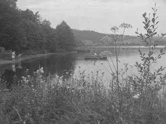 Man som fiskar i en båt på Estwaite Water och två flickor vid vattenbrynet