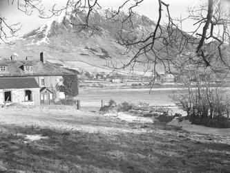 The Anglers Hotel i Ennerdale med träd i förgrunden och frusen sjö och snöiga fjäll bortom