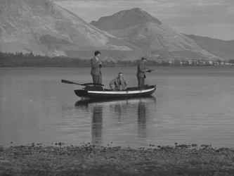 Tre män i en roddbåt på en sjö fiskar, en man är hav; havslandskap;ted, fjäll i bakgrunden