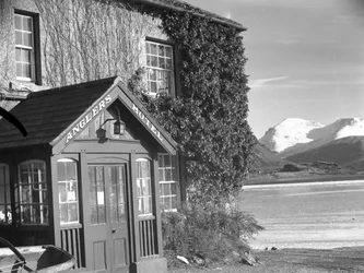 Vy över en entré till "Anglers Hotel", sjö och fjäll till höger i bild
