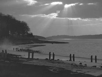 Utsikt över flodmynning mot havet; havslandskap; med gamla bryggstolpar i förgrunden och barn på gyttjeplattor i fjärran