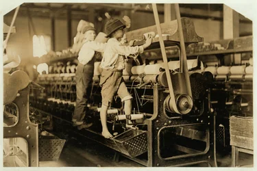 Små pojkar klättrar upp på en spinnram för att laga trasiga trådar och ersätta tomma spolar vid Bibb Mill, Macon, Georgia, 1909.