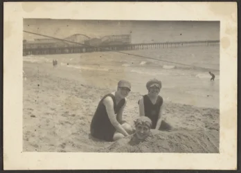 [Kvinnor på stranden som begraver en väninna i sanden]
