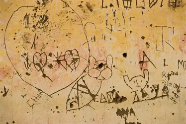 Grafitti inristad i en gammal yttre gipsvägg.