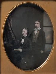Två unga män i fluga, en sittande med en bok, en stående, 1850-talet.