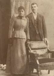 Fotografi av ett afroamerikanskt par som står bakom en stol, ca. 1890.