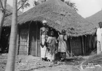 En familj framför sitt hem, Gambia, 1900-talet