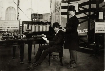 Lee DeForest (sittande) skickar ett trådlöst telefonmeddelande till Department of Electricity på 1904 års världsutställning