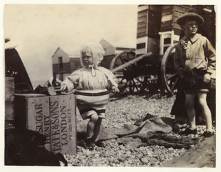 Två barn vid badmaskiner, c 1895, En ögonblicksbild av två barn vid havet, stående bland en grupp badmaskiner på stranden