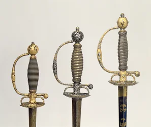 Styr av tre franska svärd: ett av stål, blått och belagt med mönster i jagat guld, ca 1730; en av stål genomborrat och mejslat och slipat av tovigt guld, c.1760; en av mejslat stål, gr