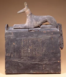 Plyonformad shabti-låda med en inskription och en staty av Anubis som en schakal (av senare datum) på locket, egyptisk, från Thebe, tidig 22:a dynastin, c.900 f.Kr. (svartmålat trä)