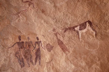 Stenkonst, förhistoria: Stenmålning av en grupp karaktärer och en tvåfärgad ko med stora horn i ett utsmyckat skydd, i Uweinat-massivet, Egypten. (Period från 8000 till 3000 år f.Kr.). Fotografi