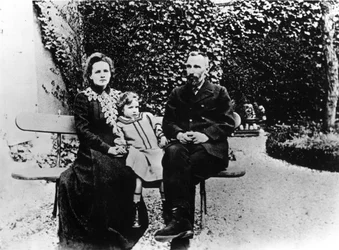 Pierre (1859-1906) och Marie Curie (1867-1934) sitter på en bänk i en trädgård.