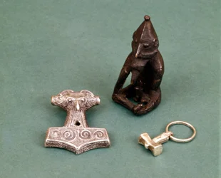 Amuletter av vikingagudar: i förgrunden två små silverhammare som symboliserar guden Tor. Statyetten föreställer Freyr, fruktbarhetsguden. Historiska museet i Stockholm, Sverige.