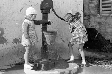 Små flickor fyller en hink med vatten, 9 maj 1939 (svartvitt foto)