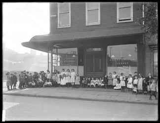 Barn poserar framför ett oidentifierat skyltfönster till Queens Borough Public Library, New York, ca 1910