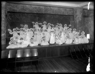 En grupp små flickor poserade på en liten scen med fans, förmodligen det romersk-katolska föräldrahemmet, Kingsbridge, Bronx, ca 1911