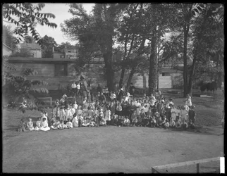 En stor grupp barn samlade för ett gruppporträtt på en oidentifierad lekplats, ca 1910