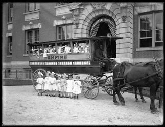 Små flickor poserar i och framför en hästdragen vagn, framför en oidentifierad byggnad, troligen den romersk-katolska föräldralösa asylen, Kingsbridge, Bronx, ca 1910