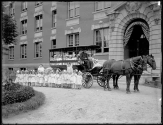 Små flickor poserar i och framför en hästdragen vagn, framför en oidentifierad byggnad, troligen Roman Catholic Orphan Asylum, Kingsbridge, Bronx, omkring 1910.