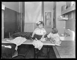 Oidentifierad liten flicka som visar hur man använder ett elektriskt strykjärn, ca 1913-14